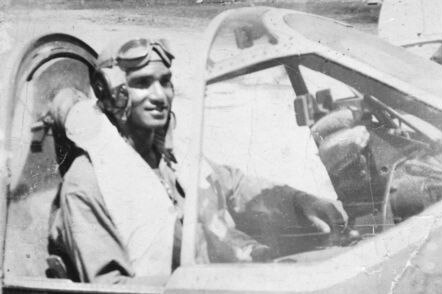 A black and white photo of an Indigenous pilot sitting in the cockpit of a plane.