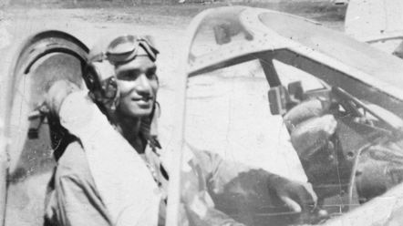 A black and white photo of an Indigenous pilot sitting in the cockpit of a plane.