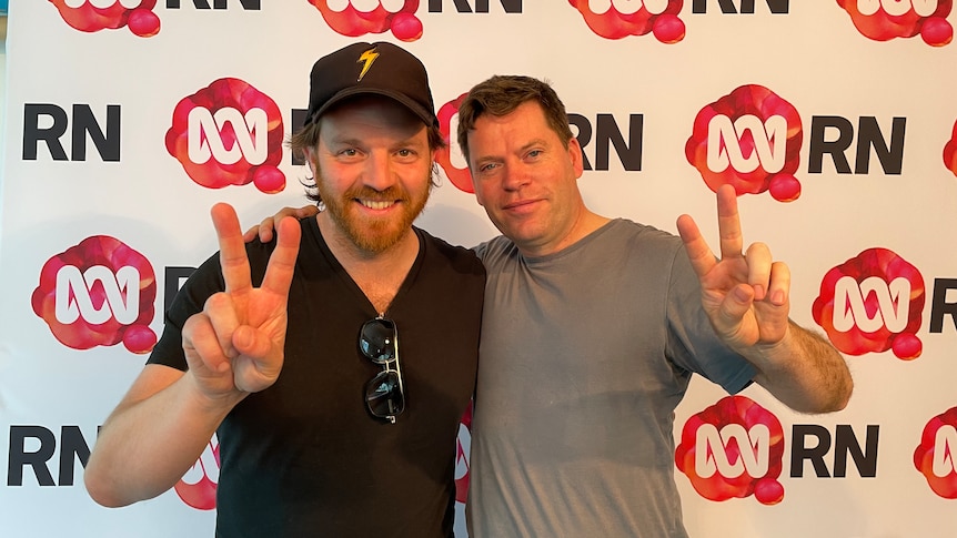 two men smile at the camer and make peace signs while side hugging 