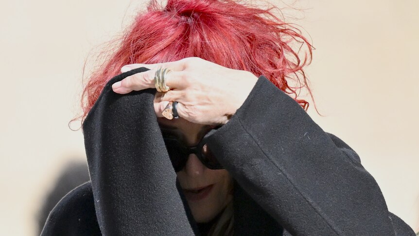 Annemie Stein with red hair covering her face with a black scarf and wearing sunglasses
