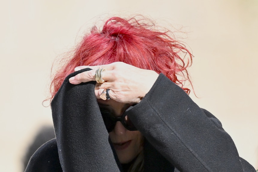 Annemie Stein with red hair covering her face with a black scarf and wearing sunglasses
