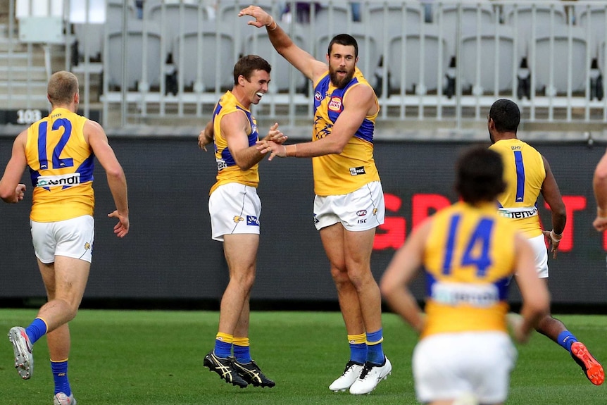 An AFL forward receives congratulations after his goal as teammates run towards him.