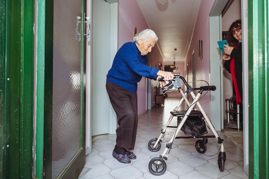 Francesca Catroppa, supported by a walking frame, dances in her home, viewed through an open front door.