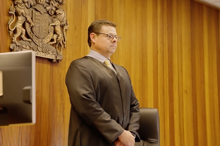 Man standing in robes in front of NSW Court emblem