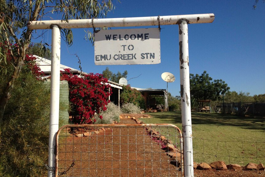 A white tin sign welcoming you to Emu Creek Station hangs on white wood before a blue sky