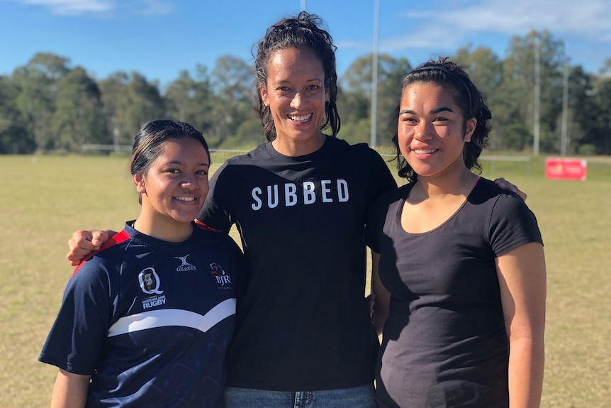Three women stand together smiling at a rugby field in Sunnybank.