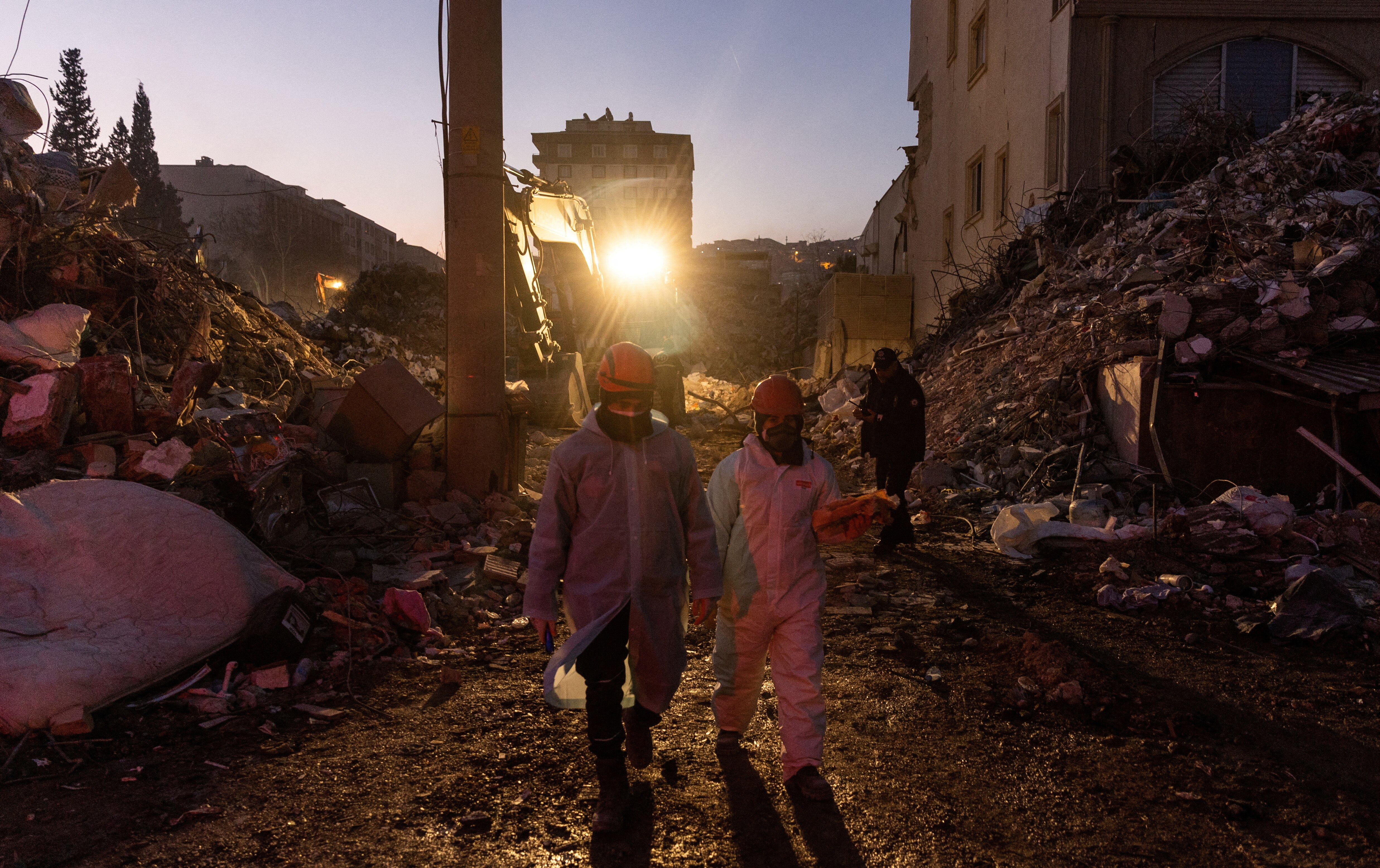 Two rescue workers walk through path in rubble.
