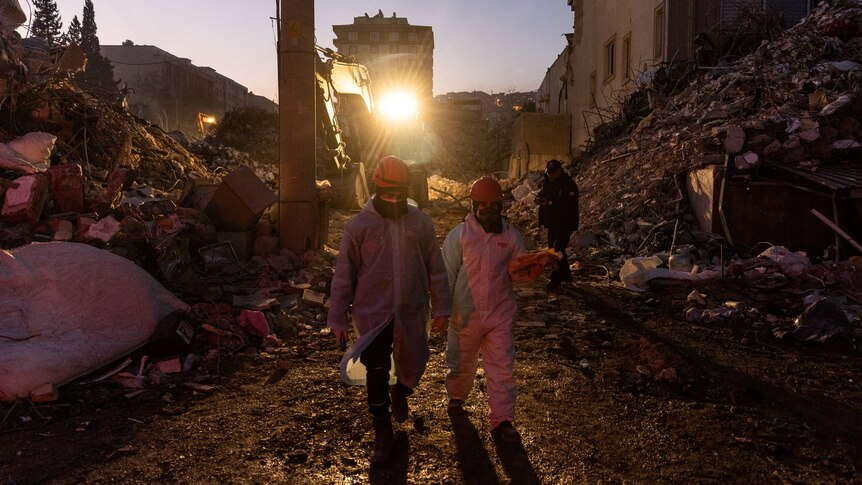 Two rescue workers walk through path in rubble.