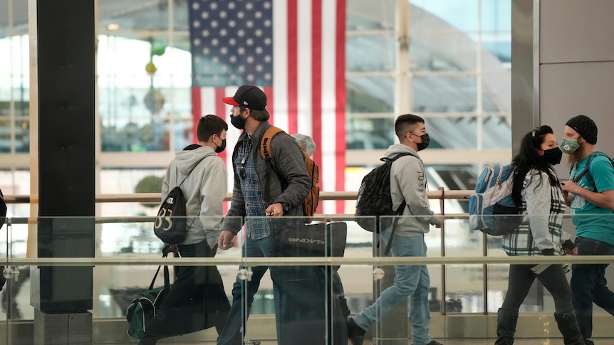 Travellers wearing face masks cross a bridge at an airport