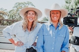Two women with blonde hair and cowboy hats on stand next to each other 