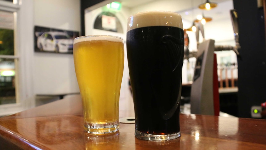 Two beer glasses sit on a bar.