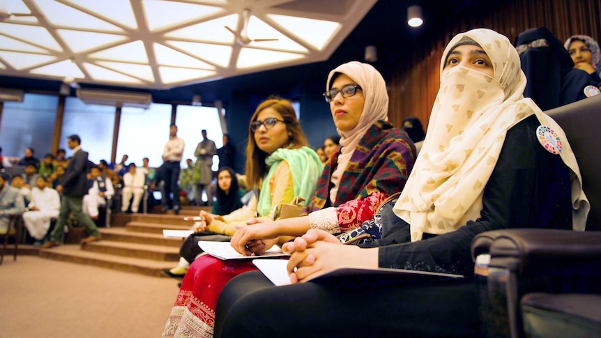 Women sit in a conference wearing hajibs and taking notes