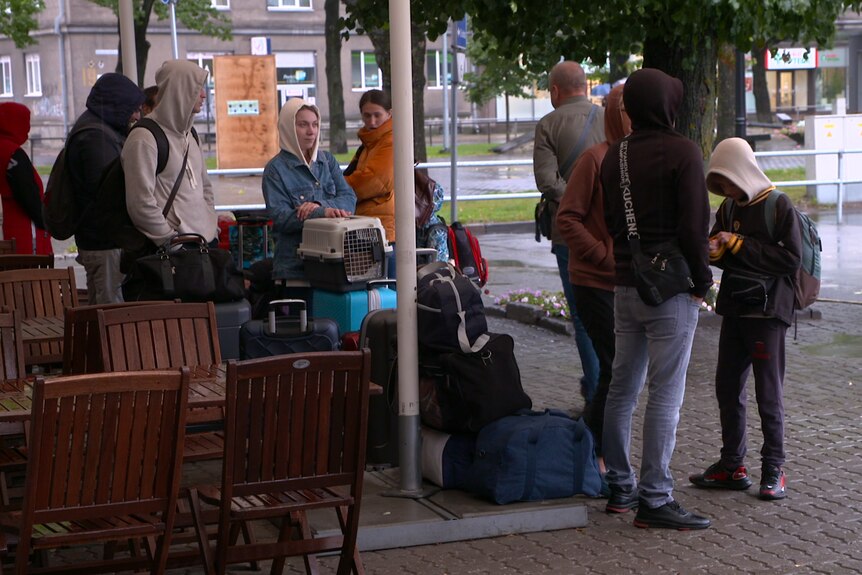 Ukrainian refugees wait at a bus stop with luggage and possesions.