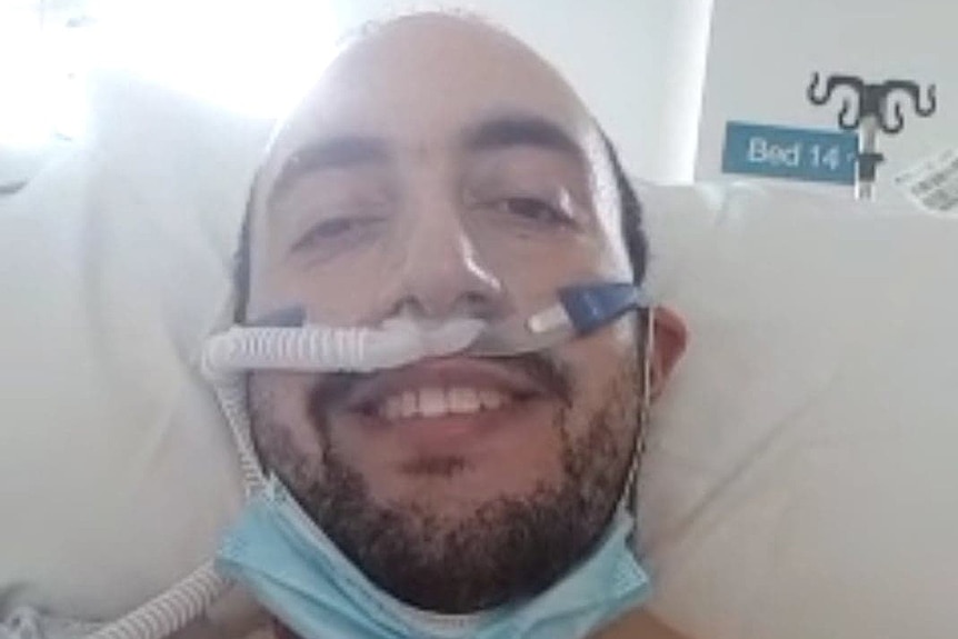 A man in a hospital bed with breathing tubes attached to his nose.