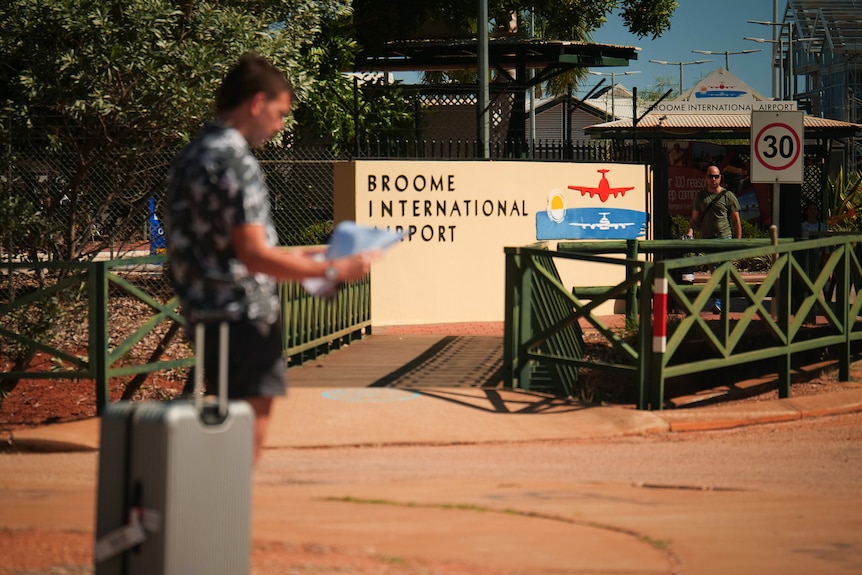 A man stands near a suitcase, looking at a map in front of a sign that says 
