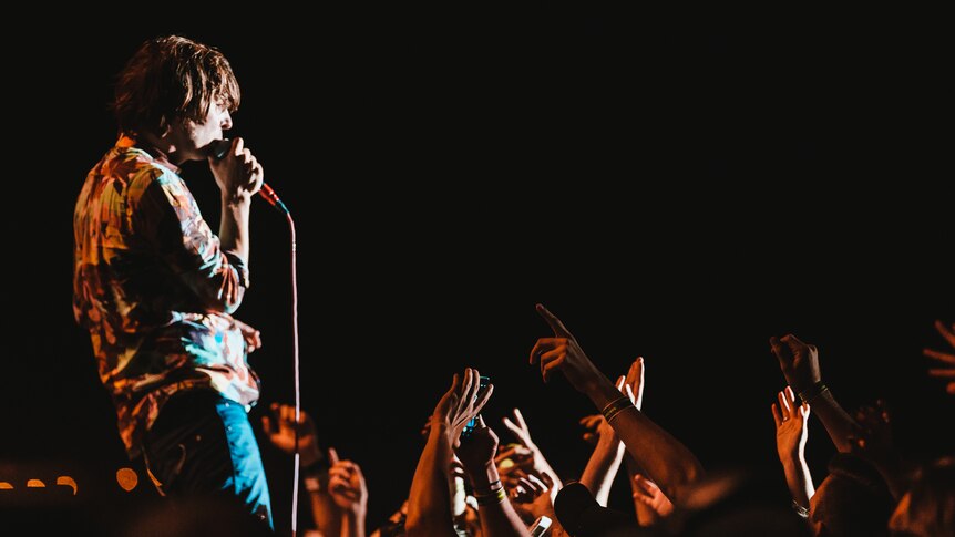 Thomas Mars from the side holding a microphone in front of s sea of outstretched arms