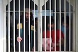 Various men look out from behind prison bars.