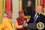 A smiling Donald Trump shakes hands with a Navajo code talker Peter MacDonald at an official ceremony.