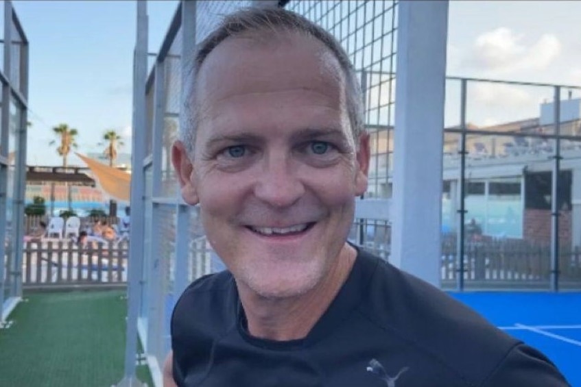 Man smiling with tennis court in the background