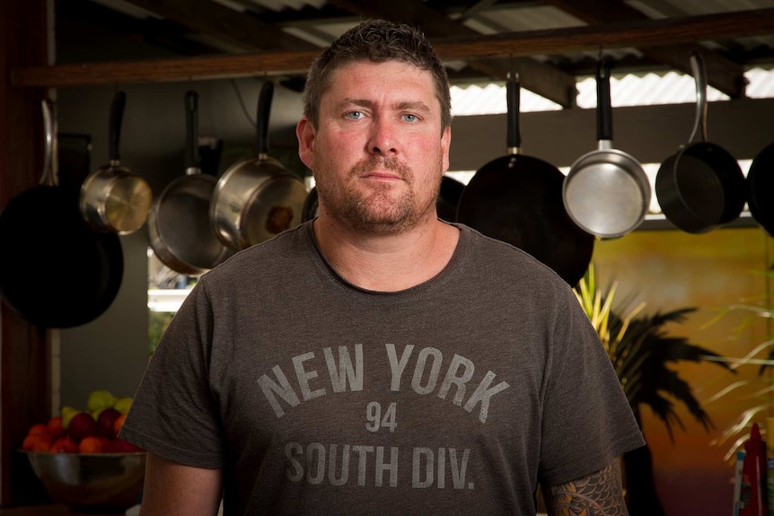 A man standing in front of pots and pans hanging up in a commercial style kitchen