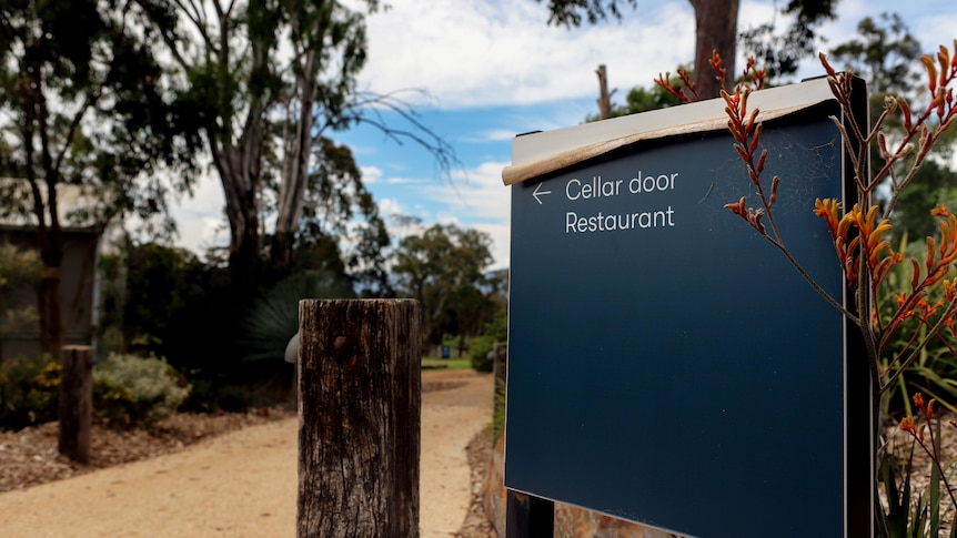 An outside sign directing to a cellar door and restaurant with trees and path in the background