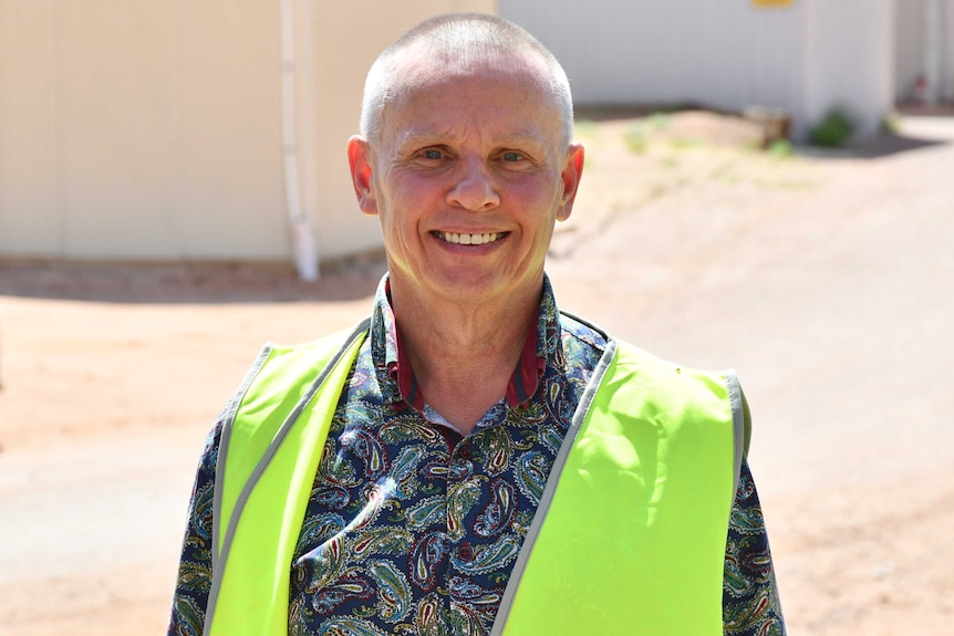 A man with short hair and a colourful shirt smiles at the camera