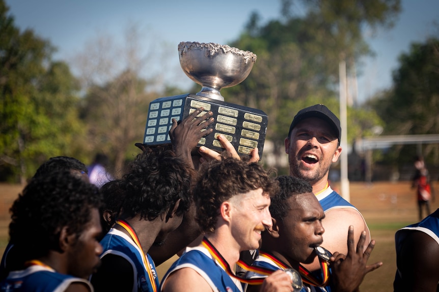 A group of players hold up a trophy at a football field.