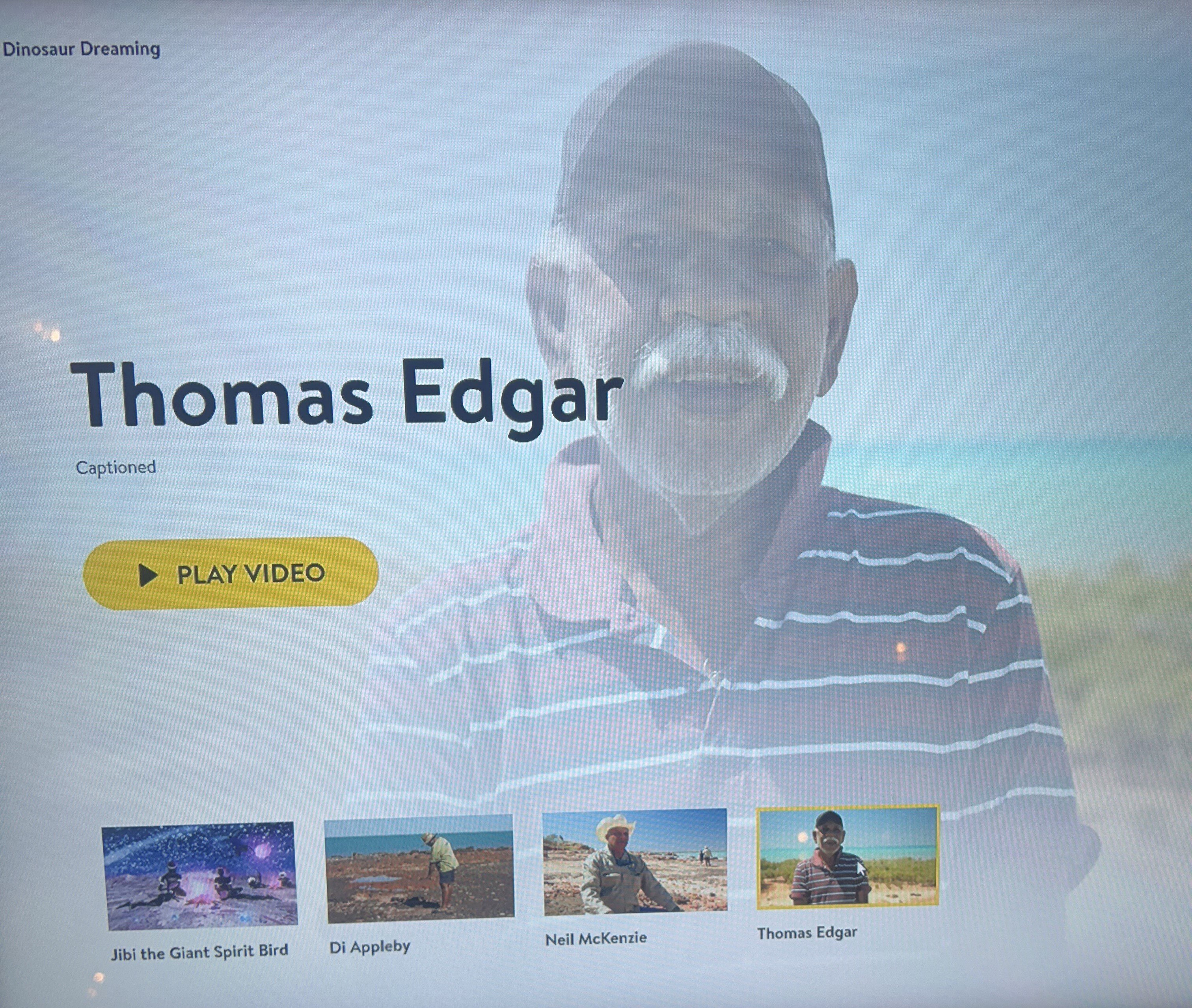 A photo of a computer screen video that says "dinosaur dreaming" and pictures a man smiling.