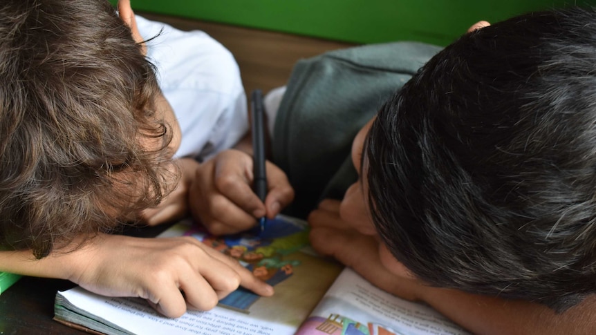 Two children drawing on a book