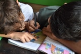 Two children drawing on a book