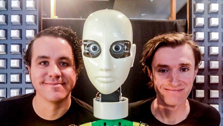 Two men stand either side of a humanoid robot