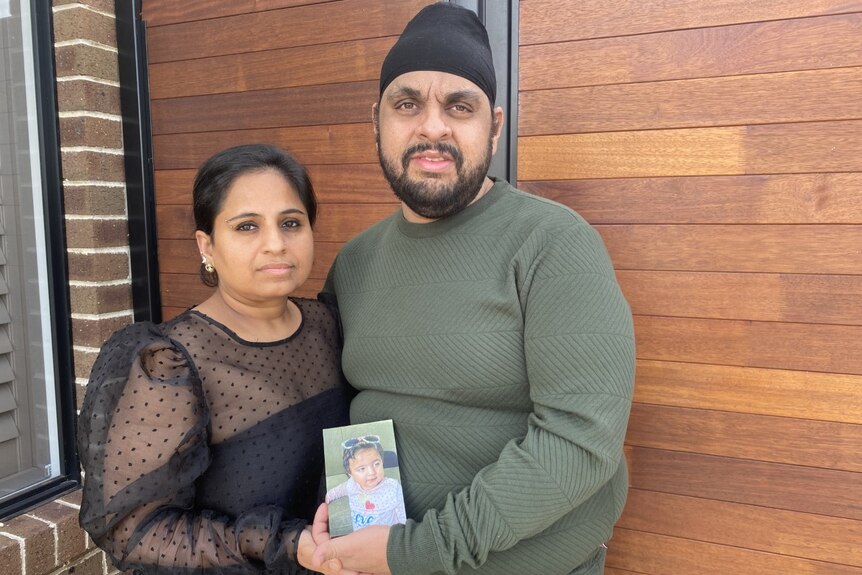 A mother and father hold up a photograph of their baby daughter. 
