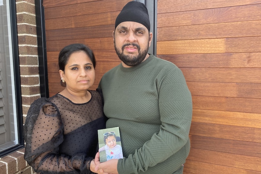 A mother and father hold up a photograph of their baby daughter. 