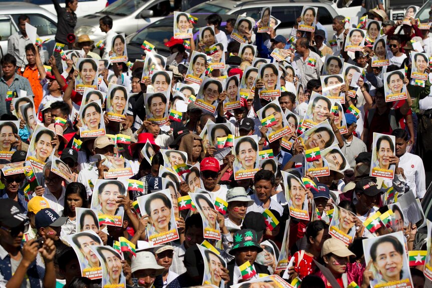 A large crowd hold posters of Aung San Suu Kyi in the air.