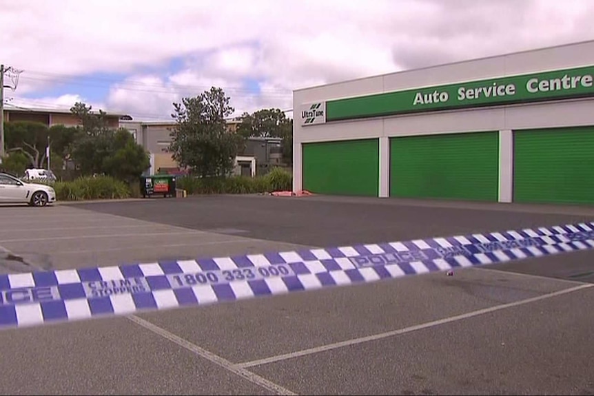 A strip of blue and white police tape in front of a large carpark and auto service centre.