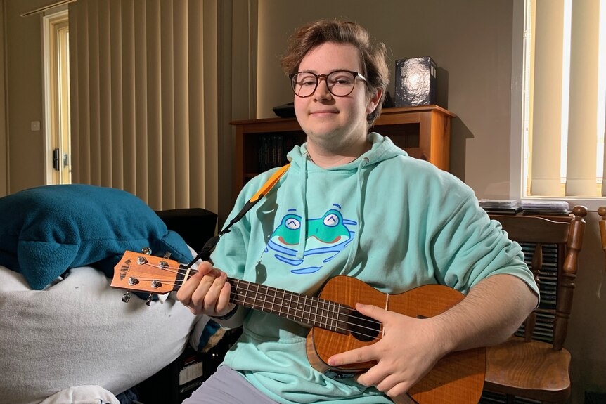 A boy holding a ukelele in a lounge room. 