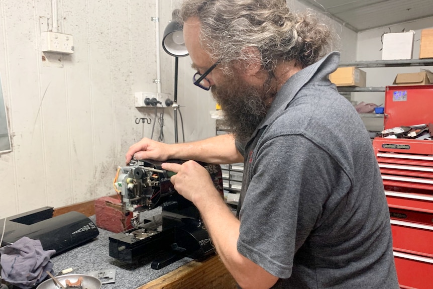 Man at an old sewing machine trying to fix it