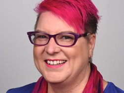 A woman with pink hair and glasses smiles