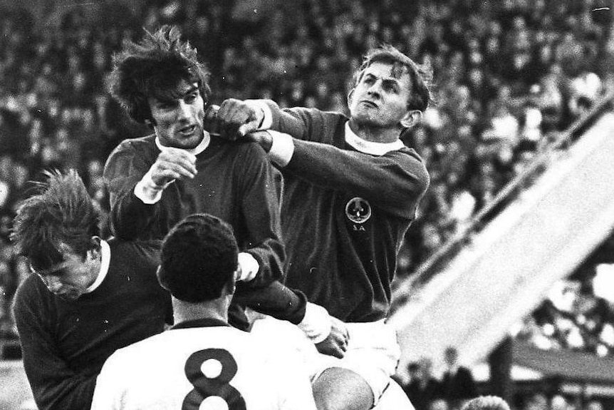 A black and white image of George BEst flying for a header in the middle of a pack of players.