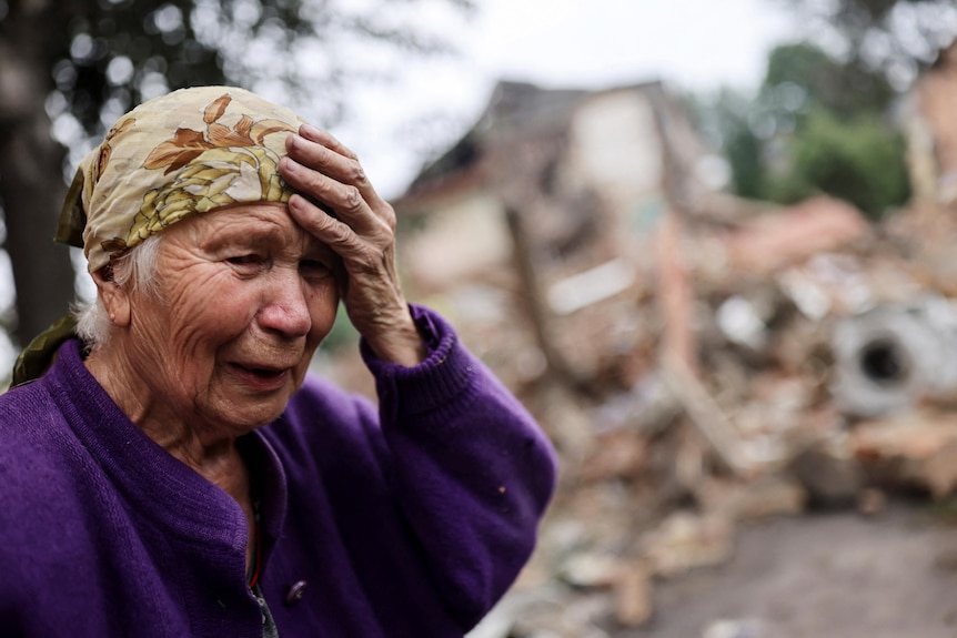 A woman in a headscarf touches her forehead and cries 