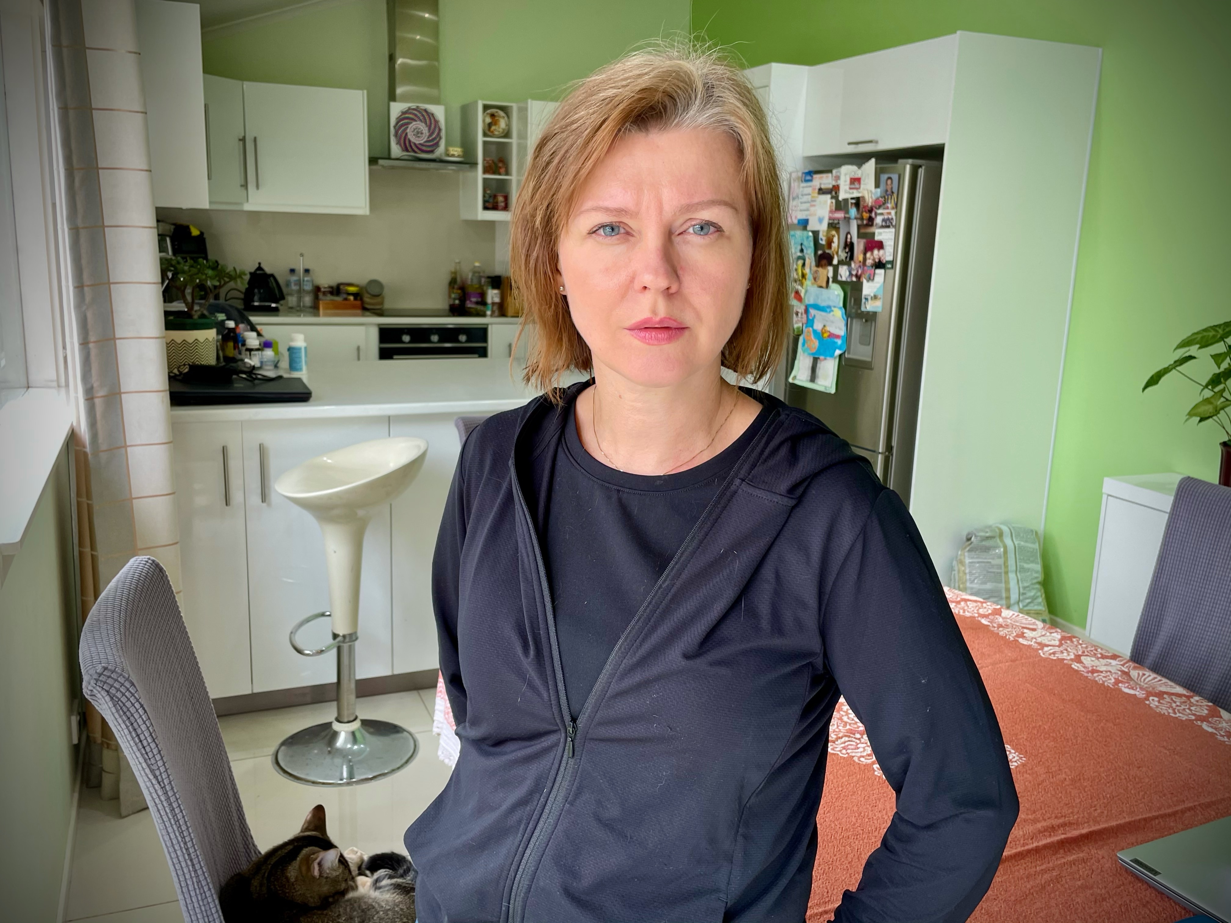 Woman wearing a navy jacket standing in a kitchen. 