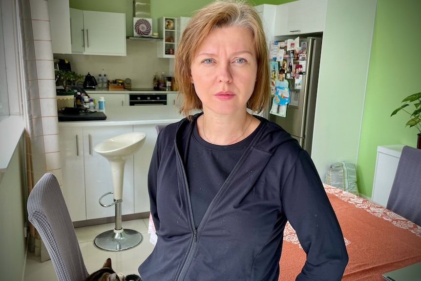 Woman wearing a navy jacket standing in a kitchen. 