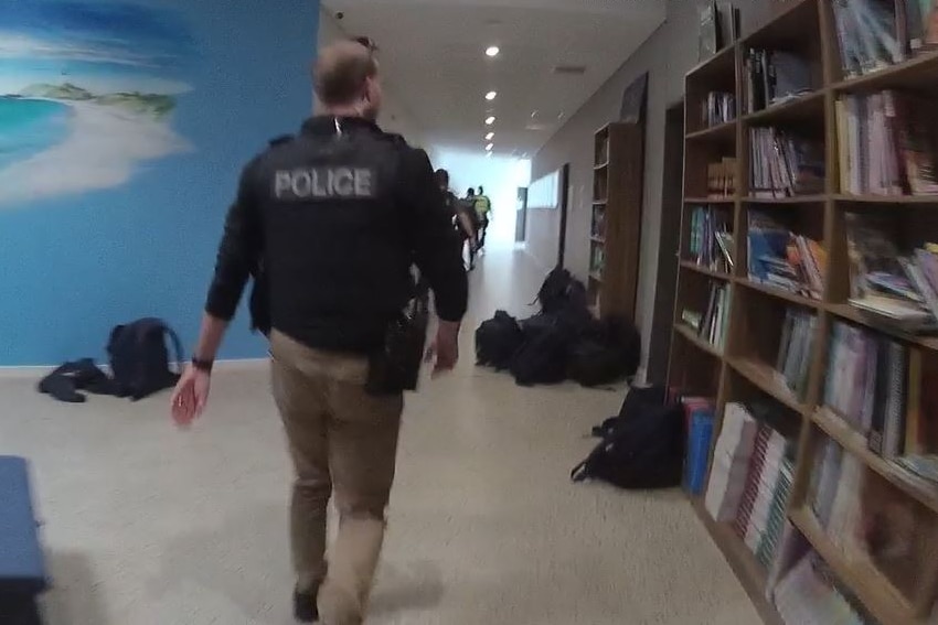 Police inside a school hallway with school bags strewn around