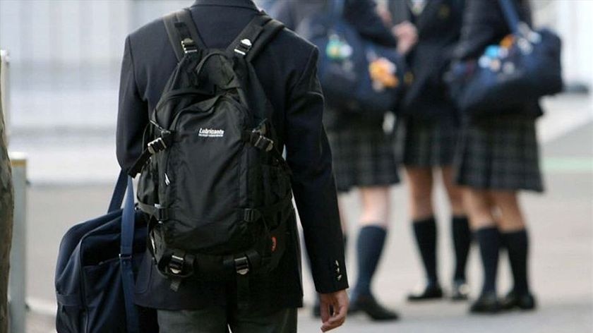 A male student is shown wearing a backpack while a group of female students are shown in the background.