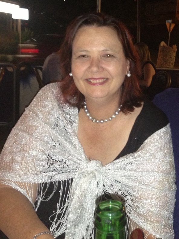 A woman smiles at the camera sitting next to a man at a dinner table. 