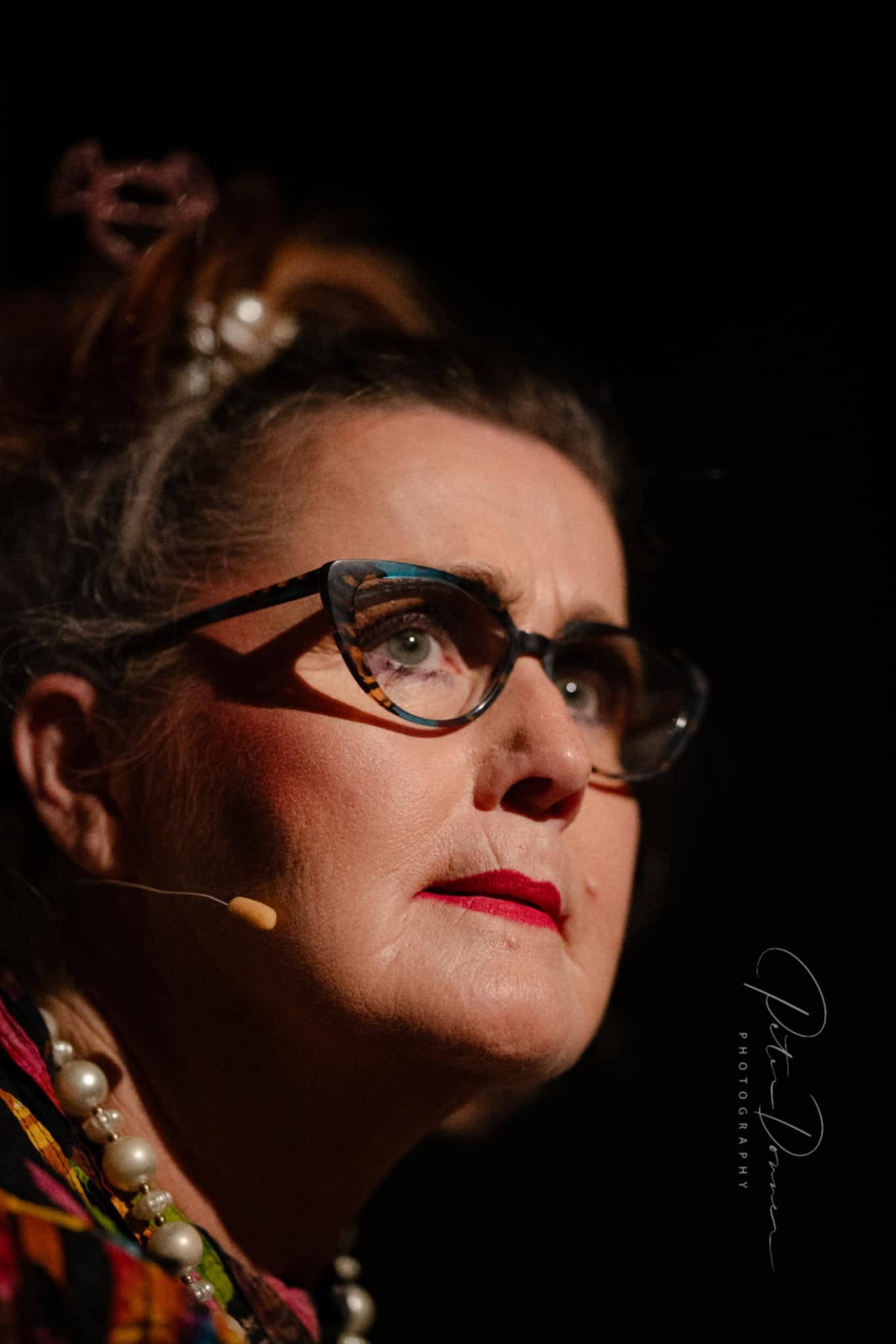Woman with glasses, red lips, and a microphone taped to her face. 