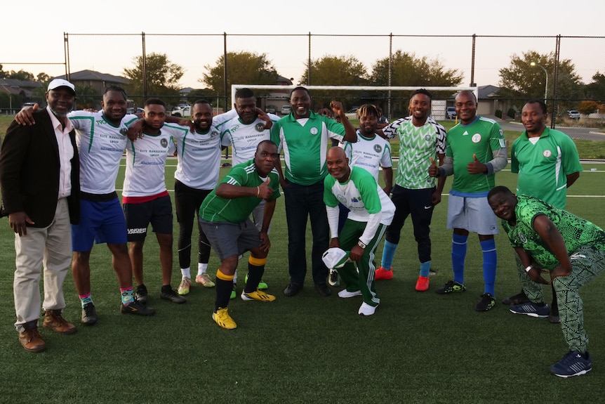 A view of a 13 Nigerian fans in a mix of green and white shirts on a synthetic field.