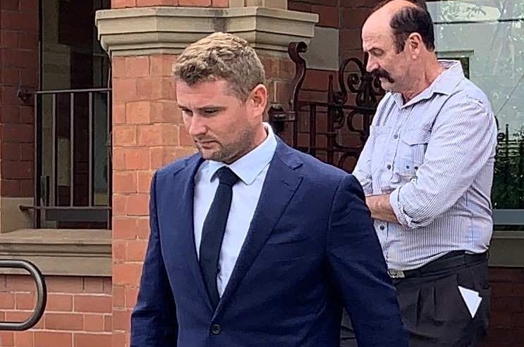 A man in a blue suit walks down steps in front of a red brick building