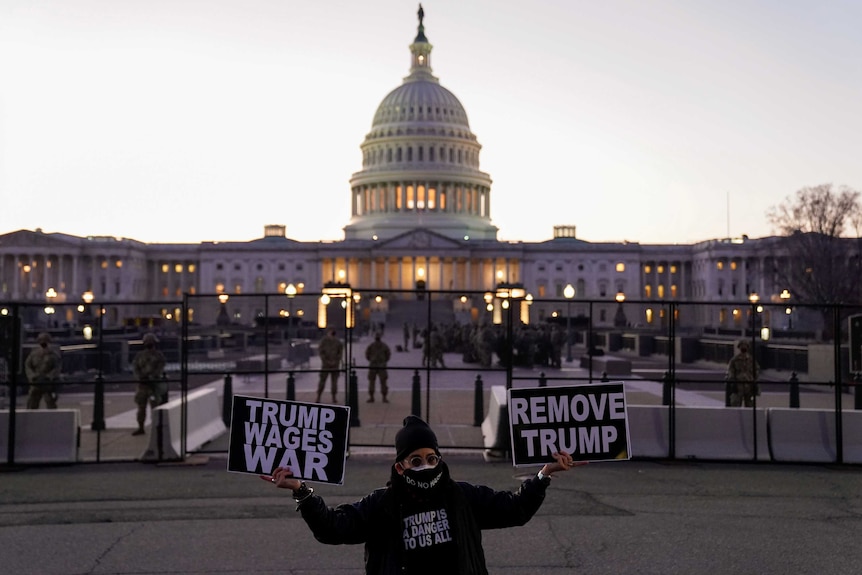 A man in a face mask holds a sign that reads "remove Trump" outside the Capitol Hill building.