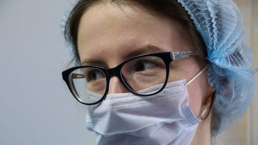 A medical worker wears a hair covering and a face mask